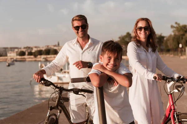 Mutlu bir aile deniz kenarında güzel bir sabah geçiriyorlar, ebeveynler bisiklete biniyor ve oğulları elektrikli scooter kullanıyor. Seçici odak — Stok fotoğraf