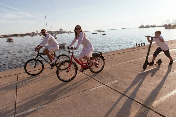 Familia feliz disfrutando de una hermosa mañana junto al mar juntos, los padres montando una bicicleta y su hijo montando un scooter eléctrico. Enfoque selectivo —  Fotos de Stock