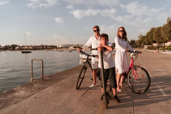 海で美しい朝を一緒に楽しむ幸せな家族、両親は自転車に乗って、息子は電動スクーターに乗っています。選択的焦点 — ストック写真