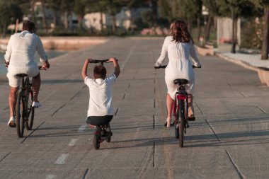 Mutlu bir aile deniz kenarında güzel bir sabah geçiriyorlar, ebeveynler bisiklete biniyor ve oğulları elektrikli scooter kullanıyor. Seçici odak 
