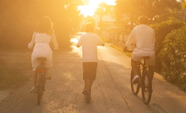 Gelukkige familie genietend van een prachtige ochtend samen, ouders die fietsen en hun zoon rijdend op een elektrische scooter. Selectieve focus — Stockfoto