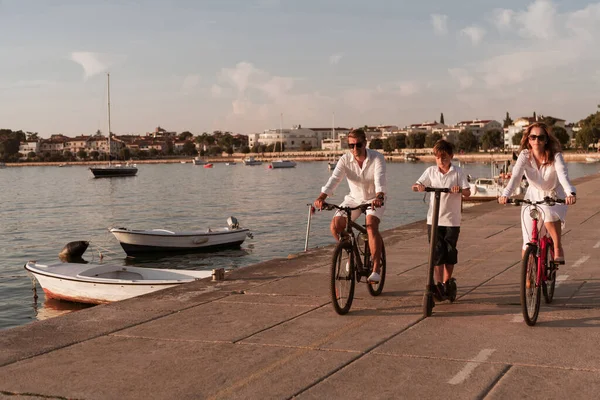 Szczęśliwa rodzina ciesząca się pięknym porankiem nad morzem, rodzice jeżdżący na rowerze i ich syn jeżdżący na skuterze elektrycznym. Skupienie selektywne — Zdjęcie stockowe