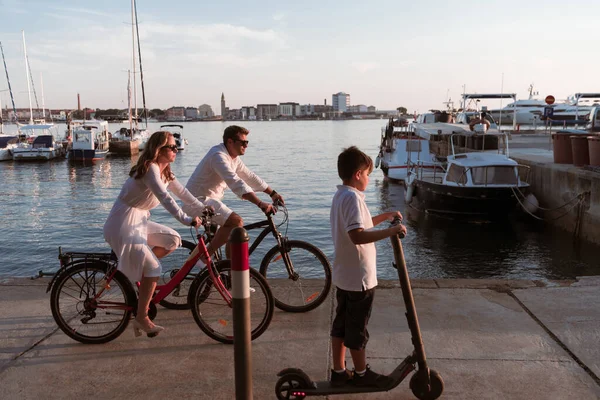 Lycklig familj njuter av en vacker morgon vid havet tillsammans, föräldrar rider en cykel och deras son rider en elektrisk skoter. Selektiv inriktning — Stockfoto