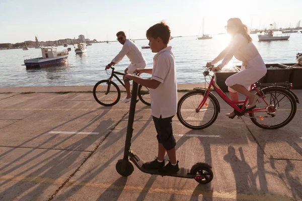 Lycklig familj njuter av en vacker morgon vid havet tillsammans, föräldrar rider en cykel och deras son rider en elektrisk skoter. Selektiv inriktning — Stockfoto