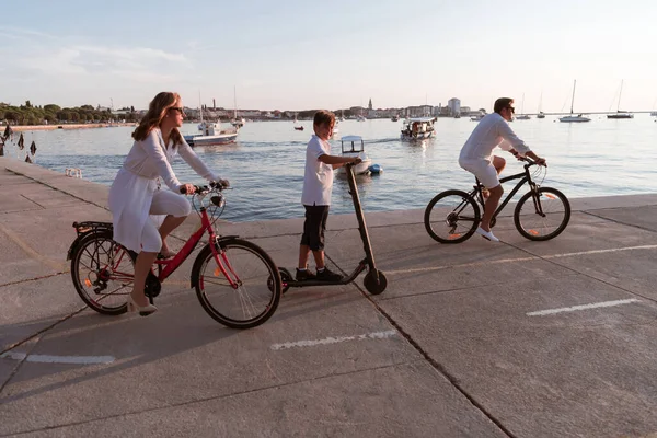 Glückliche Familie genießt einen schönen Morgen am Meer zusammen, Eltern fahren Fahrrad und ihr Sohn fährt einen Elektroroller. Selektiver Fokus — Stockfoto