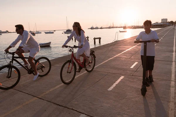 Gelukkig gezin genietend van een prachtige ochtend aan zee samen, ouders die fietsen en hun zoon die op een elektrische scooter rijdt. Selectieve focus — Stockfoto