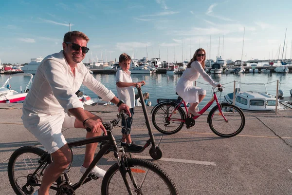 Glückliche Familie genießt einen schönen Morgen am Meer zusammen, Eltern fahren Fahrrad und ihr Sohn fährt einen Elektroroller. Selektiver Fokus — Stockfoto