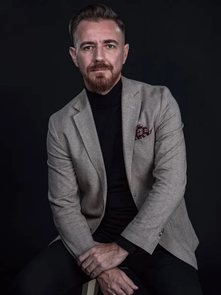 Retrato de un hombre de negocios adulto con traje de moda y sentado en un estudio moderno en una silla elegante contra el fondo negro — Foto de Stock