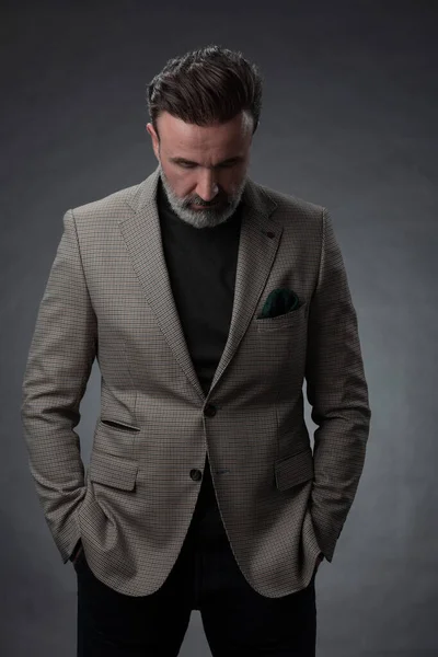 Porträtt av en elegant senior affärsman med skägg och casual business kläder i fotostudio isolerad på mörk bakgrund gester med händerna Royaltyfria Stockfoton