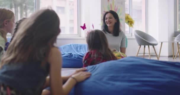 Storytime elementary or primary school teacher reading a story to a group of children in a daycare center. — Stockvideo