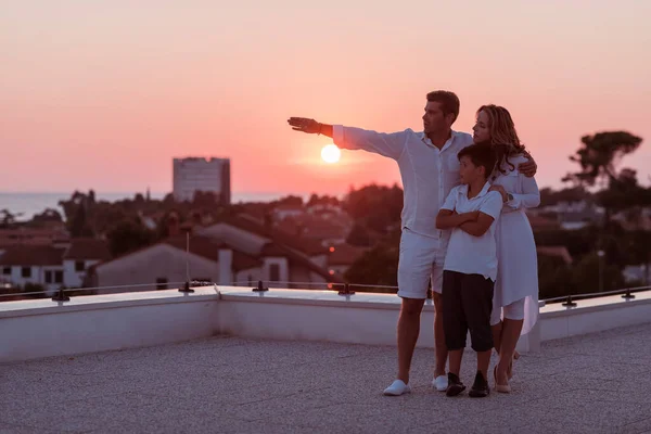 Ευτυχισμένη οικογένεια απολαμβάνει και περνά χρόνο μαζί στην οροφή του σπιτιού, ενώ βλέποντας το ηλιοβασίλεμα στην ανοιχτή θάλασσα μαζί — Φωτογραφία Αρχείου