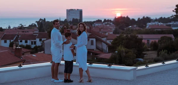 Szczęśliwa rodzina cieszy się i spędza razem czas na dachu domu, oglądając razem zachód słońca na otwartym morzu — Zdjęcie stockowe