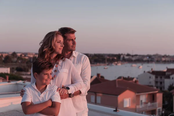 Gelukkig gezin geniet en brengt tijd samen door op het dak van het huis terwijl we samen naar de zonsondergang op de open zee kijken — Stockfoto