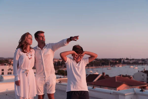 Gelukkig gezin geniet en brengt tijd samen door op het dak van het huis terwijl we samen naar de zonsondergang op de open zee kijken — Stockfoto