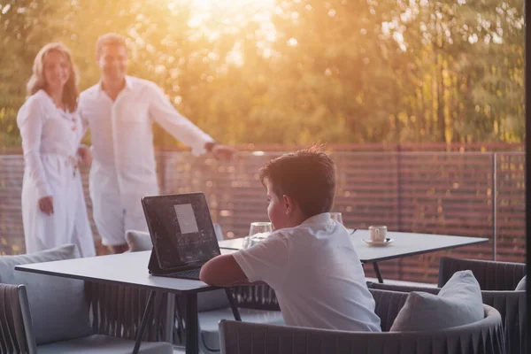 Glückliches älteres Paar, das sich auf dem Balkon eines Luxushauses ausruht, während sein Sohn ein Tablet benutzt. Selektiver Fokus — Stockfoto