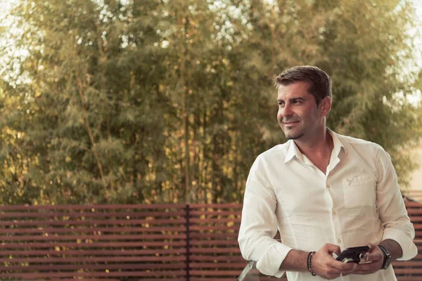 Een zakenman in casual kleding rust op het balkon van het terras tijdens het gebruik van een smartphone. Selectieve focus — Stockfoto