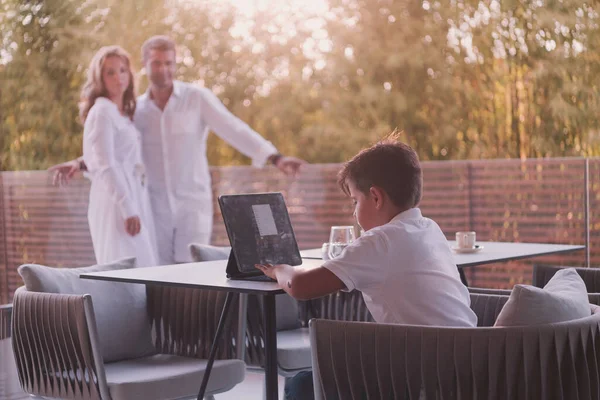 Glückliches älteres Paar, das sich auf dem Balkon eines Luxushauses ausruht, während sein Sohn ein Tablet benutzt. Selektiver Fokus — Stockfoto