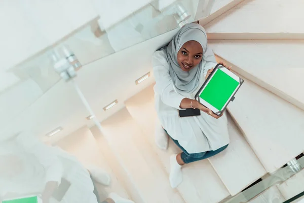 Νεαρή Αφρικανή μοντέρνα μουσουλμάνα που χρησιμοποιεί υπολογιστή tablet ενώ κάθεται στις σκάλες στο σπίτι φορώντας χιτζάμπ ρούχα πάνω όψη — Φωτογραφία Αρχείου