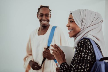 Bir grup mutlu Afrikalı öğrenci sohbet ediyor ve takım buluşması yapıyor. Ev ödevi için birlikte çalışıyorlar. Geleneksel Müslüman başörtüsü giyen kızlar.