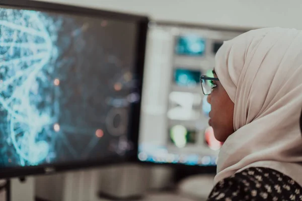 Giovane afro-americana moderna donna d'affari musulmana indossa una sciarpa in un ufficio luminoso creativo sul posto di lavoro con un grande schermo. — Foto Stock