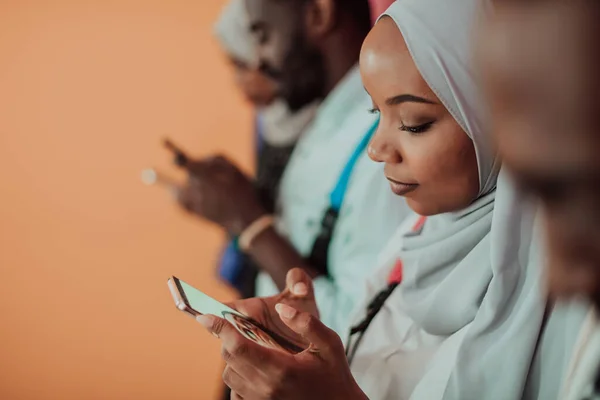 Um grupo de estudantes muçulmanos africanos usa smartphones enquanto está em frente a um fundo amarelo — Fotografia de Stock
