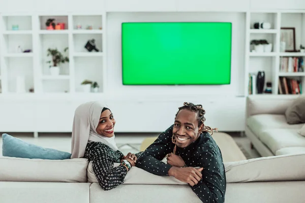 African Couple Sitting On Sofa Watching TV Together Chroma Green Screen Woman Wearing Islamic Hijab Clothes — Stock Photo, Image