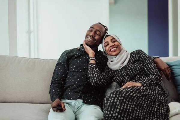 アフリカのカップルは一緒にテレビを見てソファに座っています。イスラム教のヒジャーブを着た女性 — ストック写真