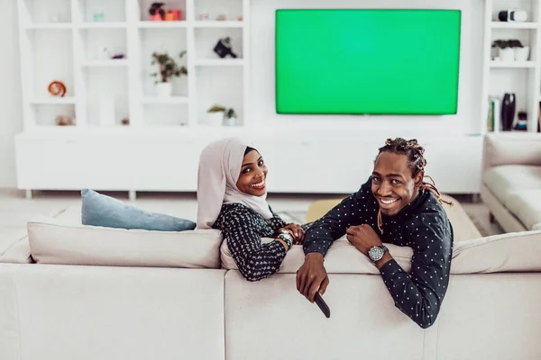 Pareja africana sentada en un sofá viendo televisión juntos Pantalla verde croma Mujer vestida con ropa islámica de Hijab — Foto de Stock