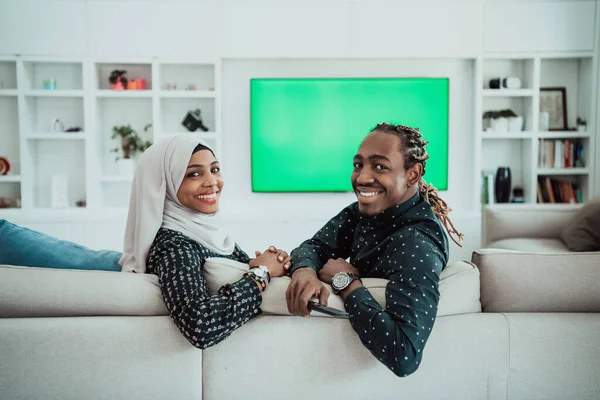 Afrikaans paar zitten op bank tv kijken samen chroma groen scherm vrouw dragen islamitische hidjab kleding — Stockfoto