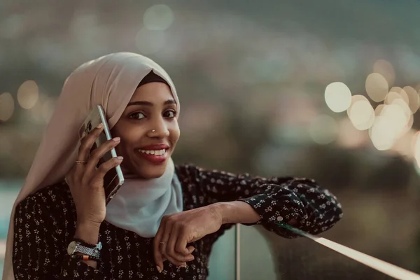 Jeune femme musulmane portant un voile d'écharpe dans la rue de la ville urbaine la nuit textos sur un smartphone avec la lumière de la ville bokeh en arrière-plan. — Photo