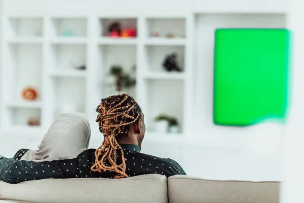 Afrykańska para siedzi na kanapie oglądając telewizję razem Chroma zielony ekran kobieta w islamskim hidżab ubrania — Zdjęcie stockowe