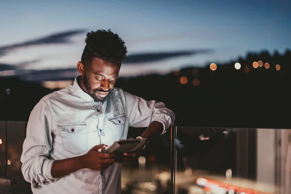 Le jeune homme dans une rue urbaine la nuit textos sur smartphone avec bokeh et néon lumières de la ville en arrière-plan. — Photo