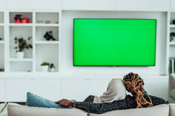 Africano casal sentado no sofá assistindo TV juntos Chroma verde tela mulher vestindo roupas islâmicas Hijab — Fotografia de Stock