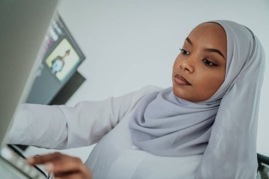 Genç Afro-Amerikalı modern Müslüman iş kadını büyük ekranlı, yaratıcı, parlak bir ofis işyerinde eşarp takıyor..