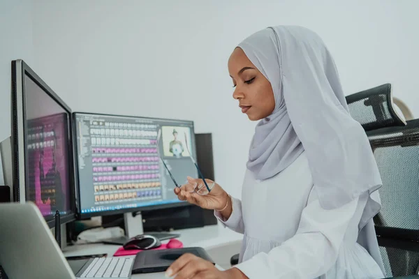 Jovem afro-americana moderna mulher de negócios muçulmana vestindo um lenço em um local de trabalho de escritório criativo brilhante com uma tela grande. — Fotografia de Stock
