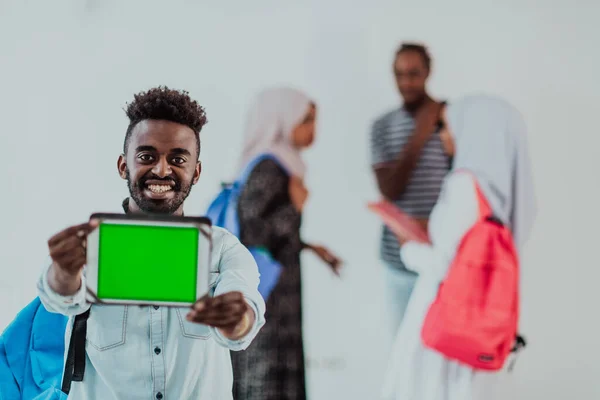 Universiteit levensstijl knappe jonge Afrikaanse student man met een tablet computer en glimlachen terwijl staan tegen de universiteit met zijn vrienden hebben een team vergadering op de achtergrond. Hoogwaardige kwaliteit — Stockfoto