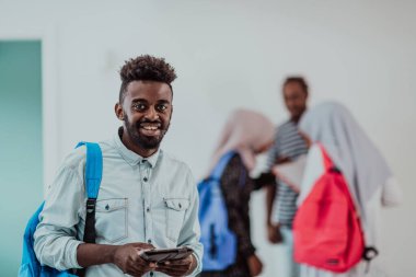Üniversite yaşam tarzı yakışıklı Afrikalı bir öğrenci elinde tablet bilgisayarla üniversitenin karşısında durup gülümserken arka planda bir takım toplantısı yapıyor. Yüksek kalite