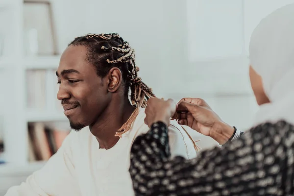 A young Muslim couple has a romantic time at home while the woman makes the hairstyle for her husband female wearing traditional Sudan Islamic hijab clothes. — Stock Photo, Image