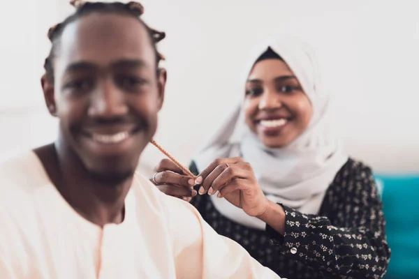 若いイスラム教徒のカップルは自宅でロマンチックな時間を過ごしていますが、女性は伝統的なスーダンのイスラムヒジャーブ服を着て夫の女性のために髪型を作っています. — ストック写真