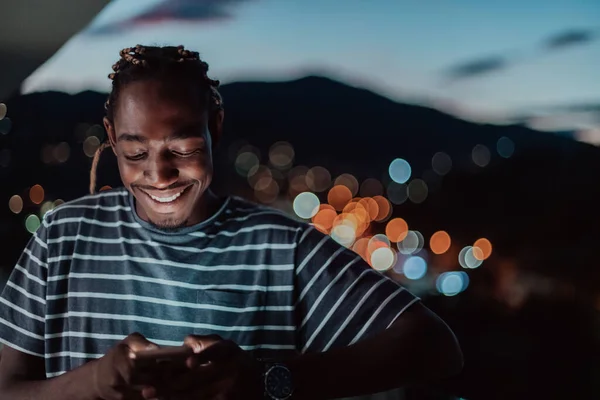 Le jeune homme dans une rue urbaine la nuit textos sur smartphone avec bokeh et néon lumières de la ville en arrière-plan. — Photo