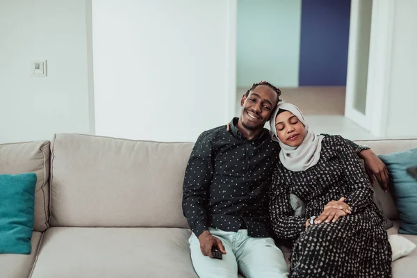 Afrikanska par sitter på soffan tittar på TV tillsammans. Kvinnan bär islamisk hijab kläder — Stockfoto