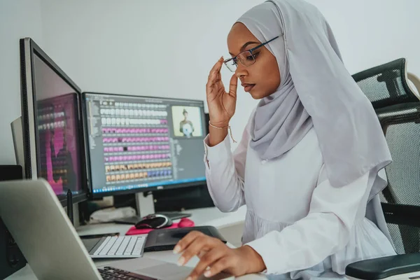 Genç Afro-Amerikalı modern Müslüman iş kadını büyük ekranlı, yaratıcı, parlak bir ofis işyerinde eşarp takıyor.. — Stok fotoğraf