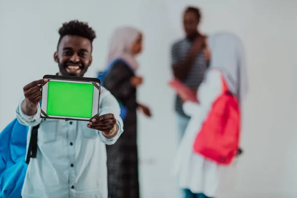 Estilo de vida universitário bonito jovem estudante africano segurando um computador tablet e sorrindo enquanto está contra a universidade com seus amigos têm uma reunião de equipe em segundo plano. Alta qualidade — Fotografia de Stock