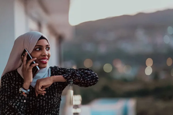 Mujer musulmana joven con velo de bufanda en la calle urbana de la ciudad por la noche mensajes de texto en un teléfono inteligente con luz de la ciudad bokeh en el fondo. — Foto de Stock