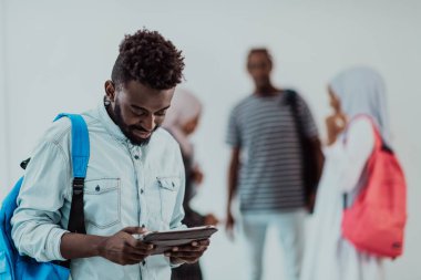 Üniversite yaşam tarzı yakışıklı Afrikalı bir öğrenci elinde tablet bilgisayarla üniversitenin karşısında durup gülümserken arka planda bir takım toplantısı yapıyor. Yüksek kalite