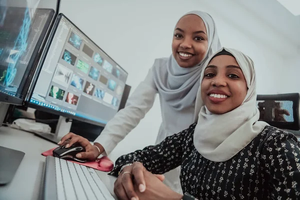 Φίλοι στο γραφείο δύο νεαρές αφροαμερικανίδες σύγχρονες μουσουλμάνες επιχειρηματίες φορώντας μαντήλι στο δημιουργικό φωτεινό γραφείο στο χώρο εργασίας με μια μεγάλη οθόνη — Φωτογραφία Αρχείου