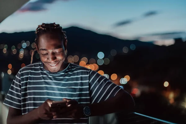 Le jeune homme dans une rue urbaine la nuit textos sur smartphone avec bokeh et néon lumières de la ville en arrière-plan. — Photo