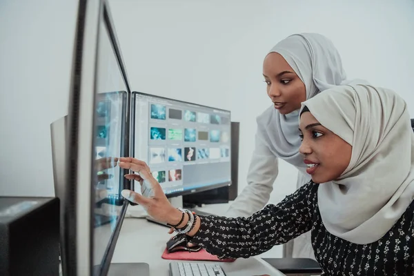 Amis au bureau deux jeunes femmes d'affaires afro-américaines musulmanes modernes portant une écharpe dans un bureau lumineux créatif avec un grand écran — Photo