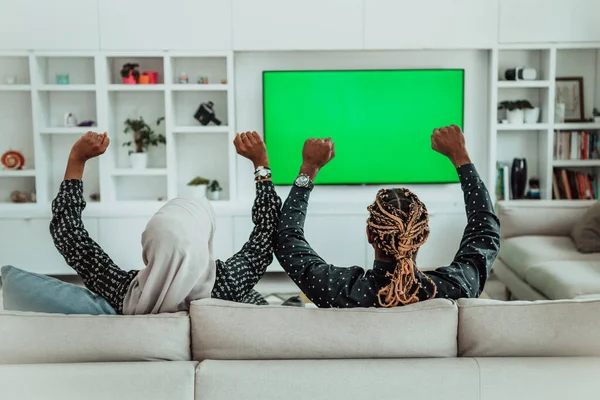 Africano casal sentado no sofá assistindo TV juntos Chroma verde tela mulher vestindo roupas islâmicas Hijab — Fotografia de Stock