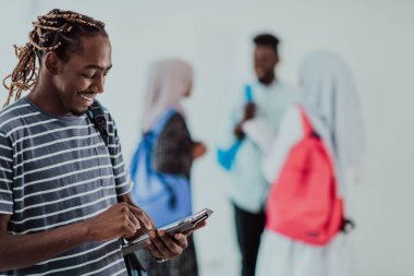 Üniversite yaşam tarzı yakışıklı Afrikalı bir öğrenci elinde tablet bilgisayarla üniversitenin karşısında durup gülümserken arka planda bir takım toplantısı yapıyor. Yüksek kalite